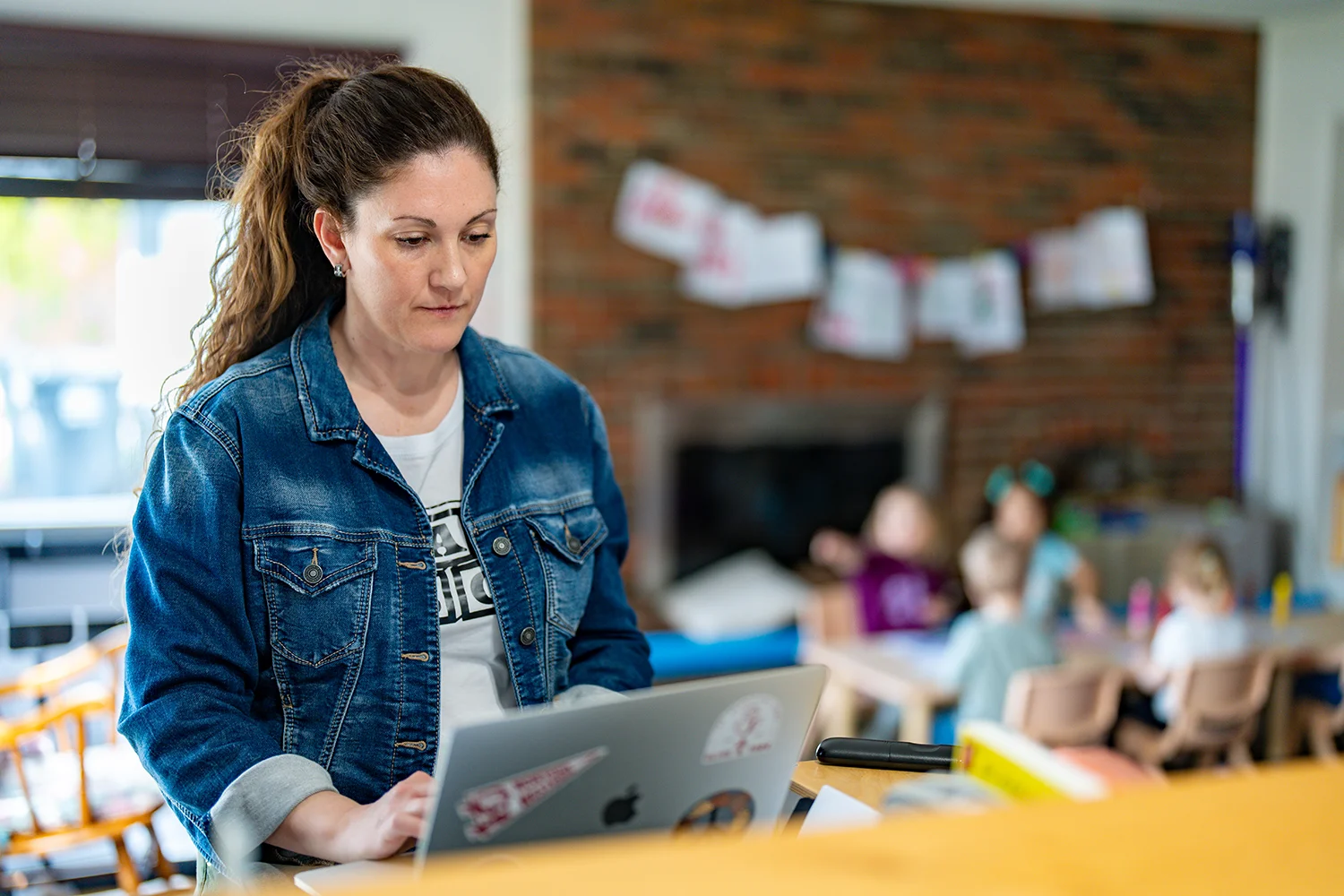 Amy Paden, plAyBCs owner, works on her computer while her assistant leads a group of children in learning